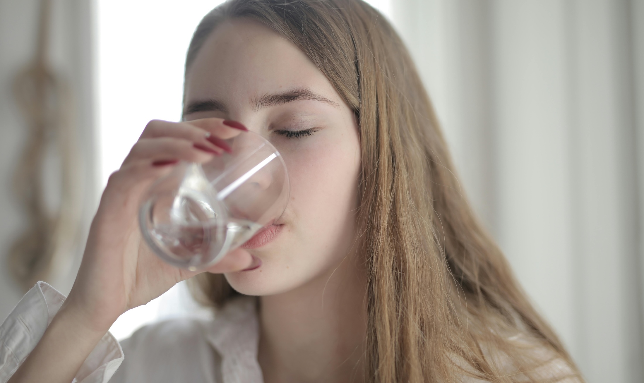 Young white woman with long dirty blond hair drinking a glass of water