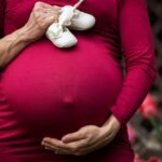 Pregnant person holding belly and baby shoes